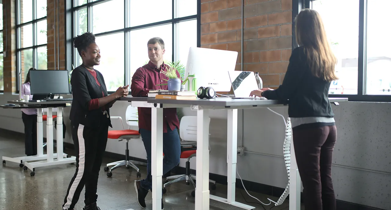 Three colleagues collaborating at a standing desk in an open office